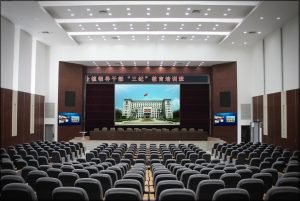 Auf dem Foto ist ein großer bestuhlter Raum zu sehen. Am Ende des Raumes ist eine Bühne mit chinesischen Schriftzeichen.