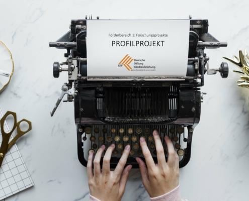 Auf dem Foto ist eine Schreibmaschine zu sehen. Im Gerät steckt ein Blatt mit dem Text "Profilprojekt":