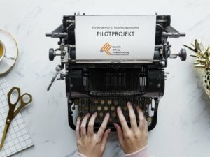 Auf dem Foto ist eine Schreibmaschine zu sehen. Im Gerät steckt ein Blatt mit dem Text "Pilotprojekt":